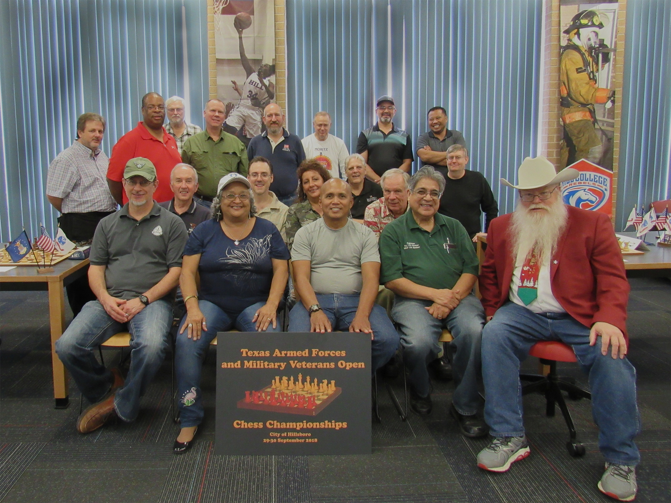 2018 Texas Armed Forces and Military Veterans Open Chess Championships.  First Row (seated from left to right):  Air Force Veteran Bret Lynn; Texas Armed Forces Women’s Champion Clarese Roberts; Oklahoma Armed Forces and Army Champion Neil Naputo; Army Veteran Carmen Chairez; Texas Armed Forces Champion Jim Hollingsworth.  Second Row (seated from left to right):  Texas Military Veterans Champion Charles Fricks; Games Judge Jeffrey Spyrison; Texas Armed Forces Student Champion Sheryl McBroom; the Adjutant, Air Force Retiree Dale Chaney.  Third Row (standing from left to right):  Chief Tournament Director and Champion Texas Hold-um Player Chris Wood; Army Veteran Leon Toliver; Chess Expert and Texas Legacy Champion Ron Farrar; Georgia Armed Forces Chess Champion, Retiree Champion and Chess Expert David Hater.  Third Row (seated from left to right):  Army Veteran Troy Gillispie; Chess Expert and Marines Champion John Ferrell.  Fourth Row (standing left to right):  Cal Chess Armed Forces and Life Member Champion Tom Boyd; Texas Chess Association President and Texas Armed Forces Navy Champion Tom Crane; Air Force Champion Jimmy Nazario; Texas Armed Forces Unrated Champion Jedwayne Bowser.  Group photo by Joe Shaughnessy.