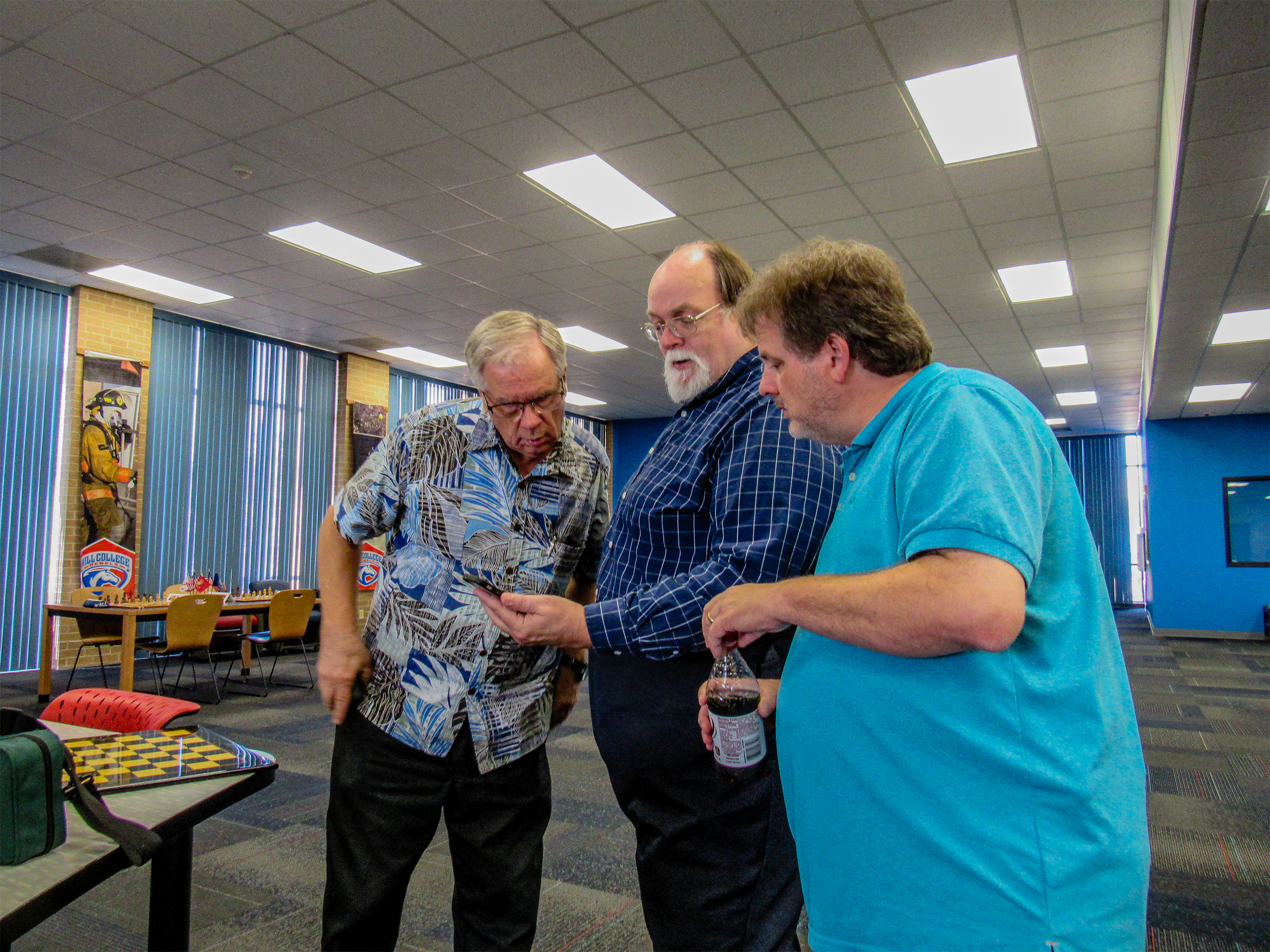 During Friday afternoon's set-up Adjutant Dale Chaney, Library Director Joe Shaughnessy, Chief Tournament Director Chris Wood paused to look at a new chess app on a phone.  Photo by Jim Hollingsworth.