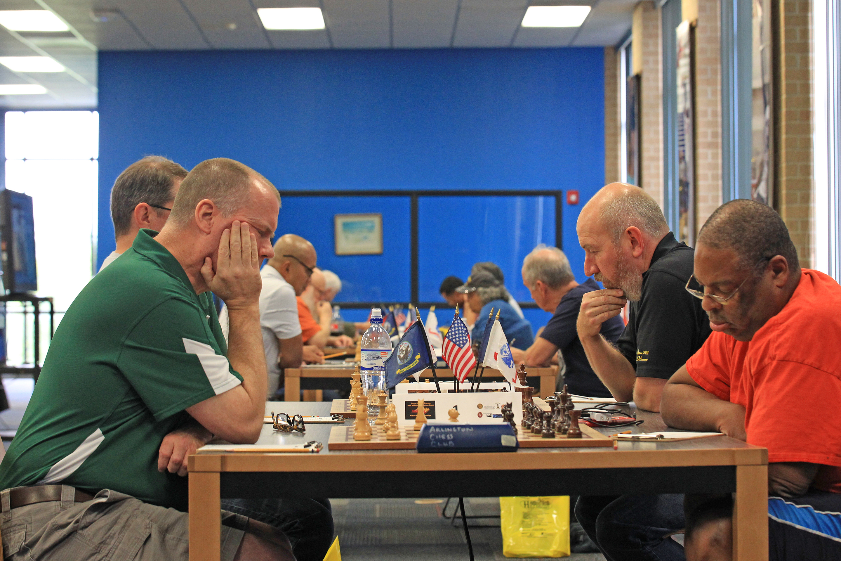 Round One and Board One (closest).  Chess Expert Ron Farrar (left wearing green) and Leon Toliver (right wearing orange).  On Board Two (behind Leon Toliver) is Chess Expert David Hater (wearing black).  Photo by Sheri Hemrick.